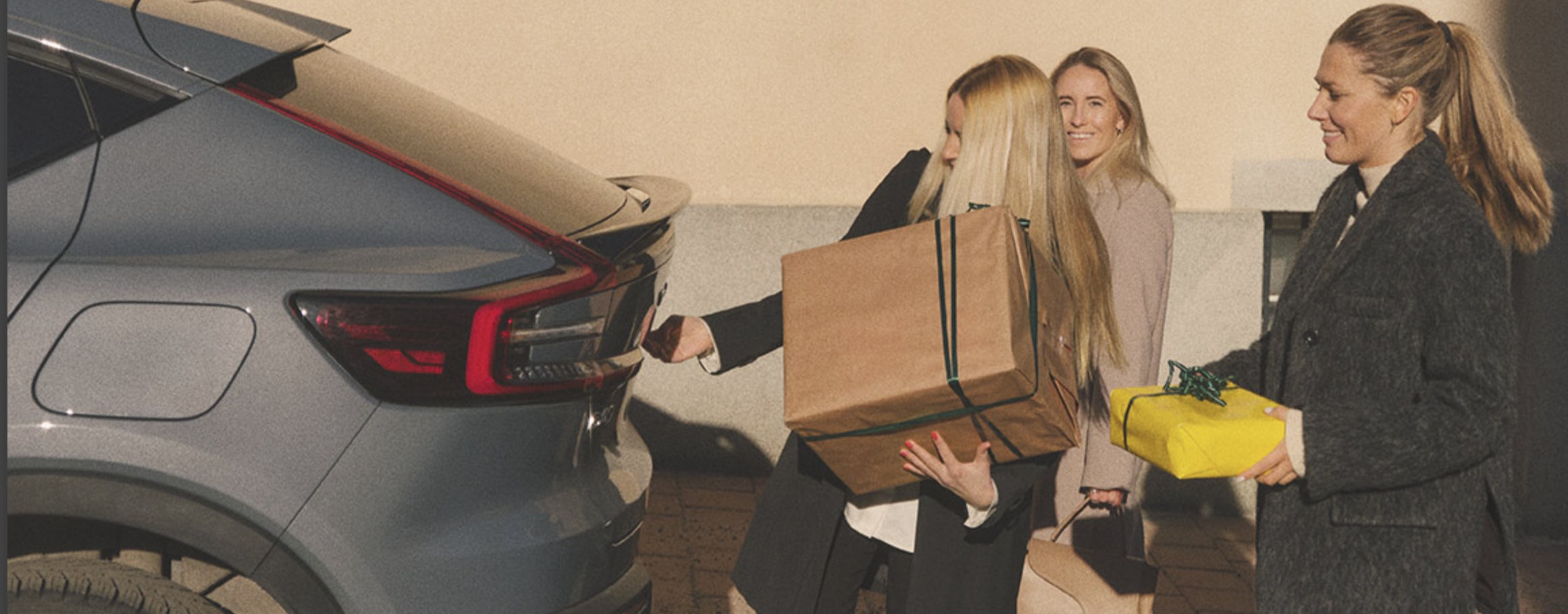 Tre kvinnor med inslagna paket påväg att lastas i en Volvo.