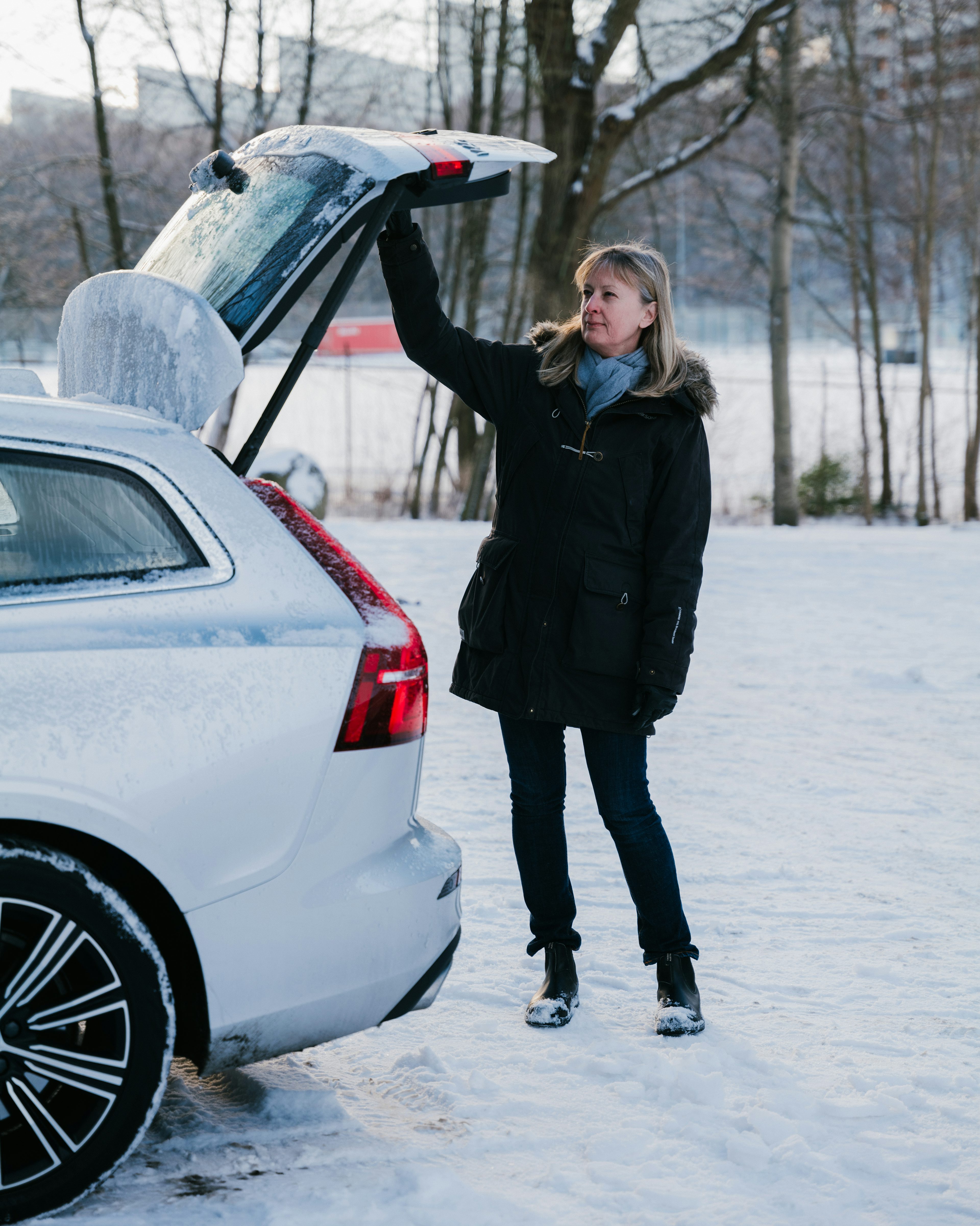 En kvinna i en vinterjacka öppnar bakluckan på en Volvo som står parkerad på snötäckt mark.