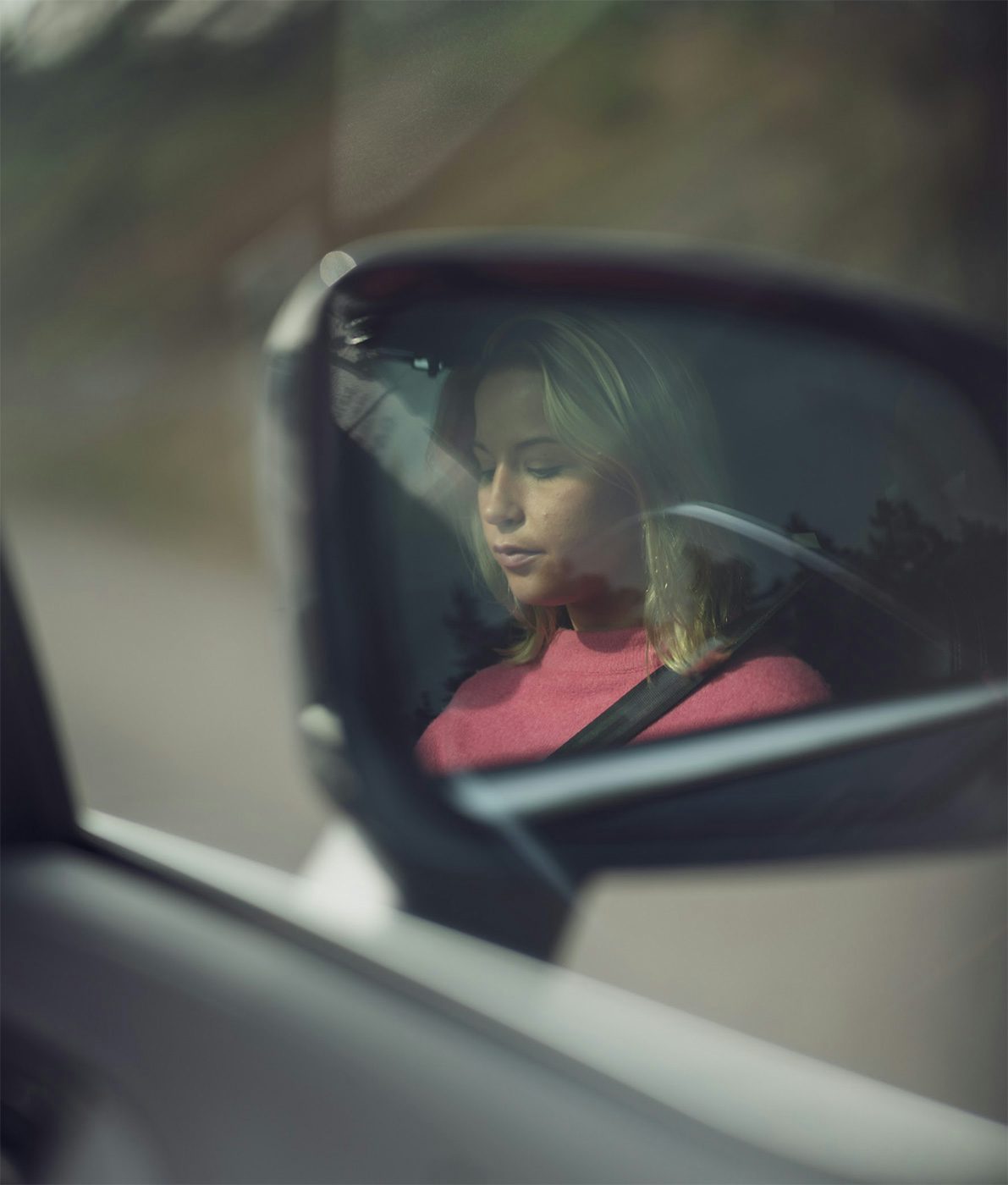 En kvinna i en rosa tröja reflekteras i en bils sidospegel.