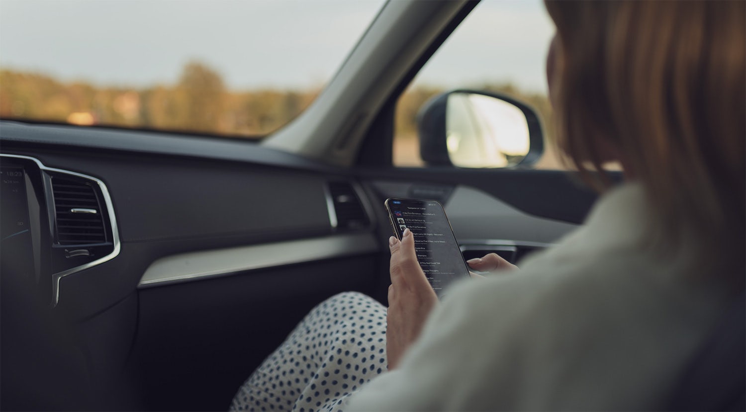 En kvinna som tittar på sin smartphone i passagerarsätet på en Volvo.
