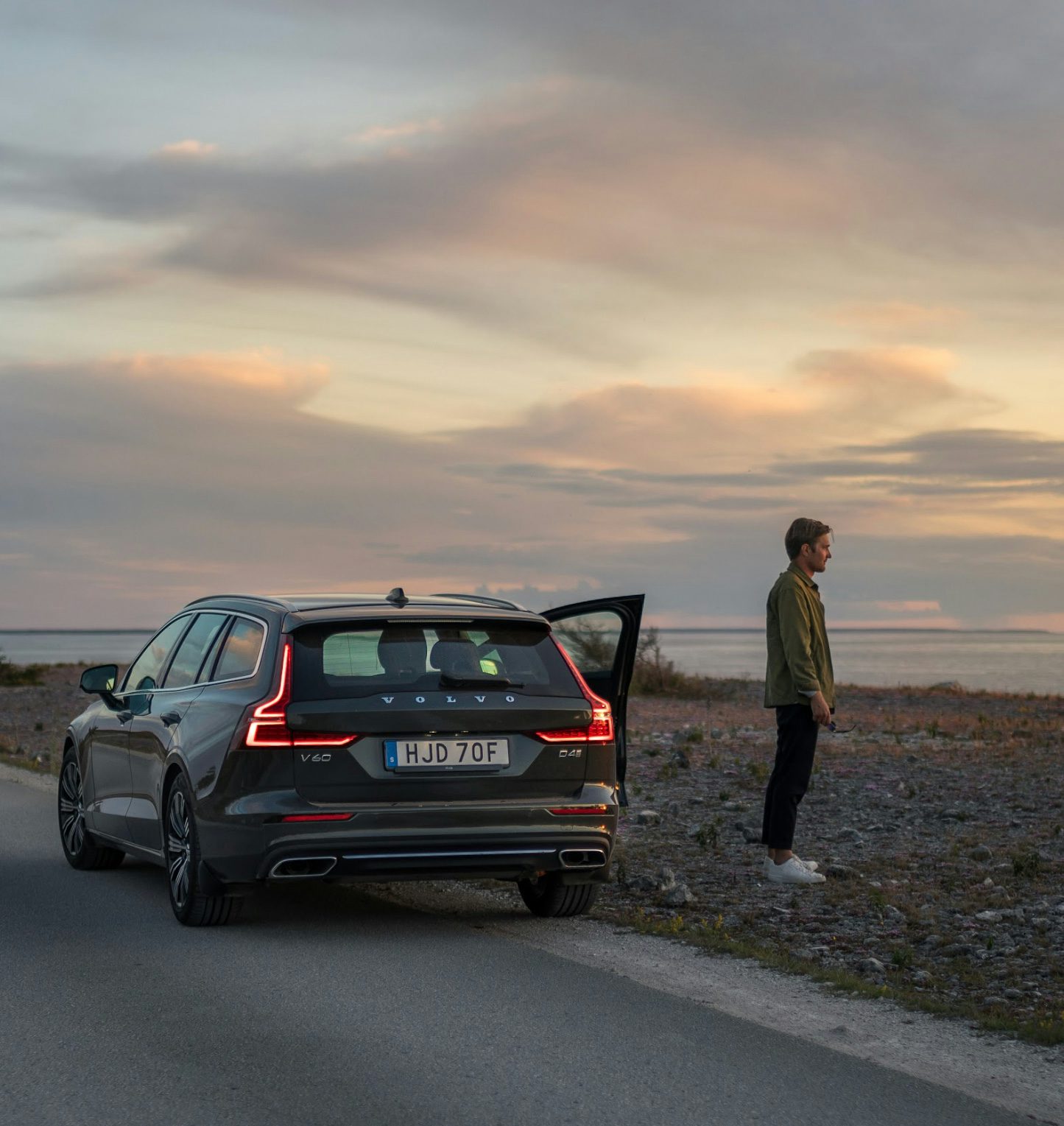 Volvo V60 parkerad på en kustväg vid solnedgången med en man som betraktar horisonten