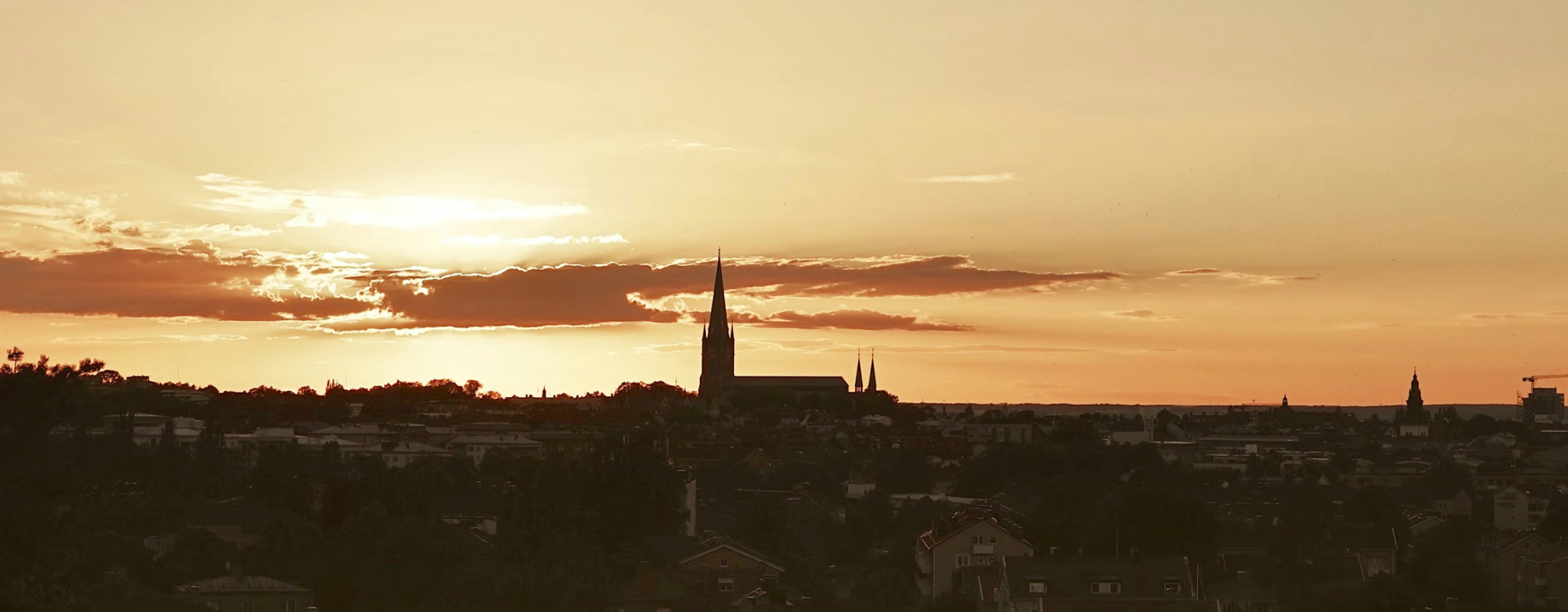 Solnedgång över Linköpings stadssilhuett med dramatisk himmel och kyrkans torn som utmärker sig mot horisonten